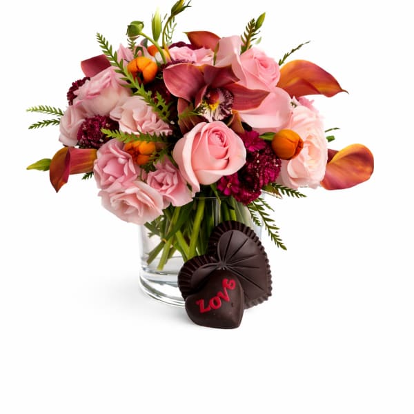 Pink and burgundy floral bouquet in a glass vase with chocolate hearts
