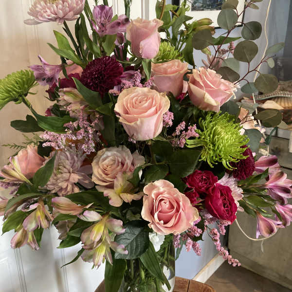 Mixed pink and purple bouquet in a clear glass vase with a pink ribbon