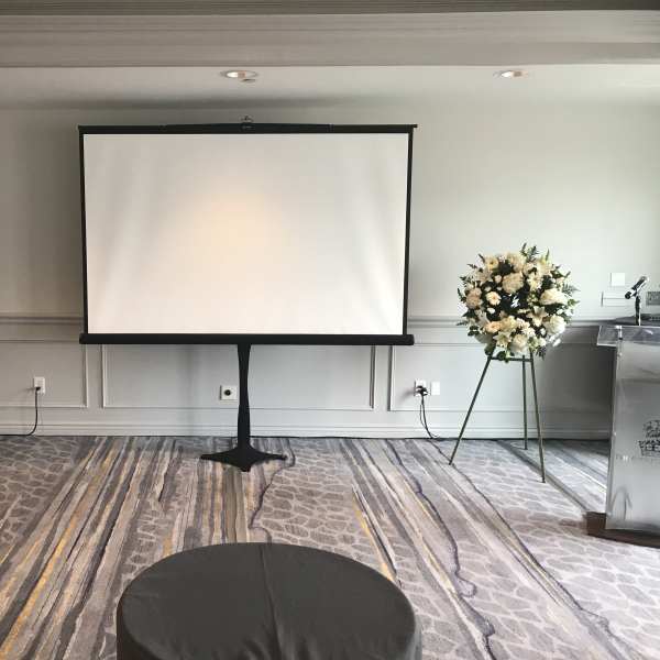 Two white floral standing arrangements flank a projection screen in a room