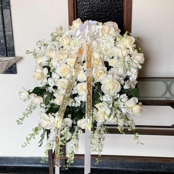 Large white rose funeral spray with ribbon streamers on a stand