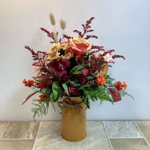 Mixed bouquet in a gold tin vase with orange, burgundy, and yellow flowers