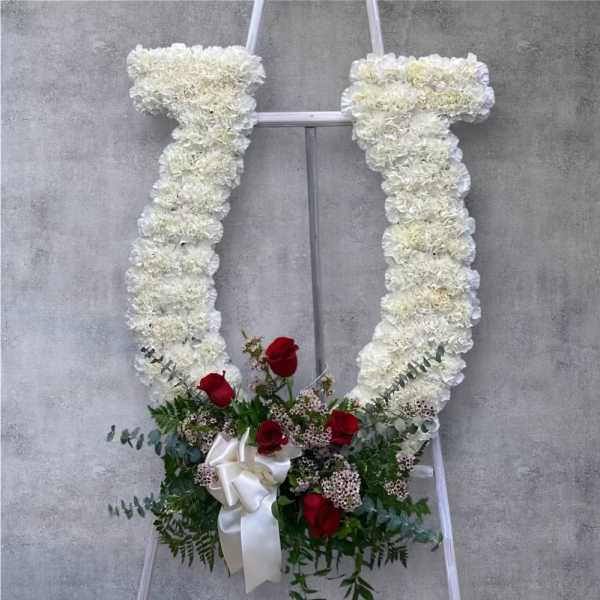 White floral standing spray with red roses and a white ribbon