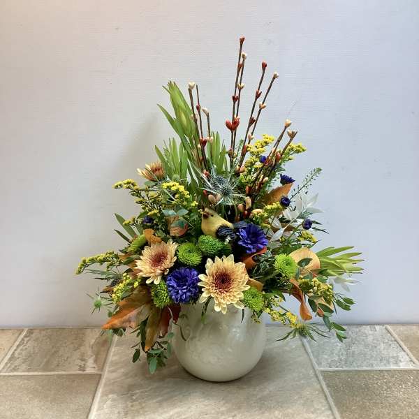 Mixed floral arrangement in a white vase with yellow, purple, and cream blooms