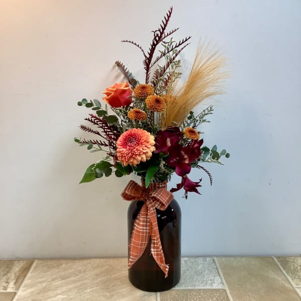 Mixed orange and burgundy floral arrangement in a dark vase with a plaid ribbon