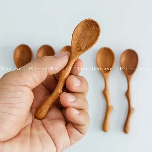Hand holding a small wooden spoon with more spoons in the background