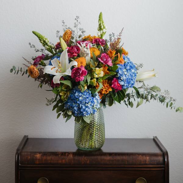 Colorful mixed bouquet in a green glass vase with lilies and hydrangeas