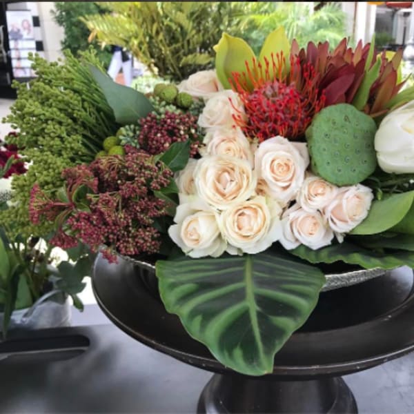 Mixed floral arrangement with cream roses, white tulips, and green tropical accents in a black pedestal bowl