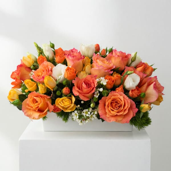 Orange, pink, yellow, and white roses in a white rectangular vase