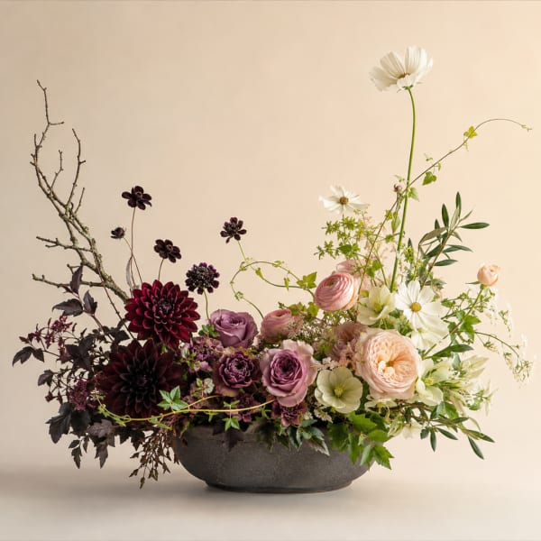 Low floral arrangement in a dark bowl with pink, white, and burgundy blooms