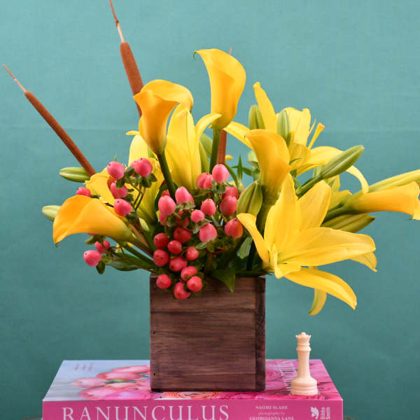Yellow calla lilies and pink berries in a wooden box vase