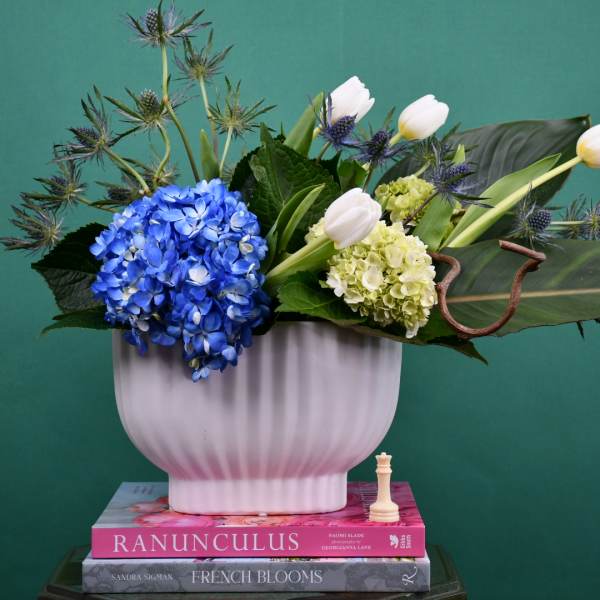 Blue hydrangea and white tulips in a white vase with spiky thistle accents