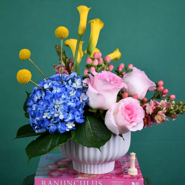 Mixed bouquet in a white vase with blue hydrangea, pink roses, and yellow calla lilies