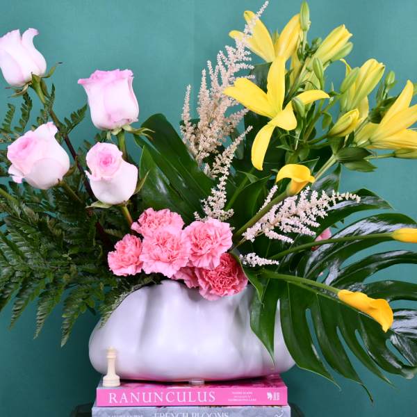 Pink roses and yellow lilies in a white vase with fern foliage
