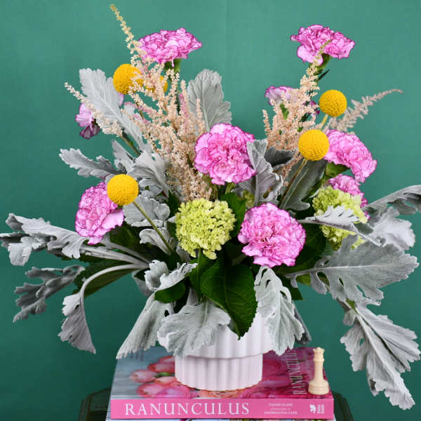 Pink carnations and yellow billy balls in a white vase
