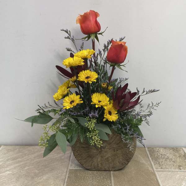 Arrangement of red roses and yellow daisies in a round wooden container