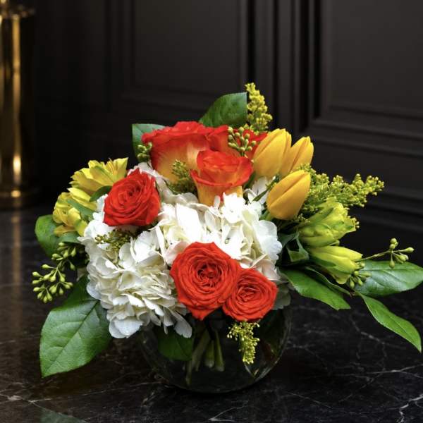 Bouquet of red roses, white hydrangeas, and yellow tulips in a glass vase