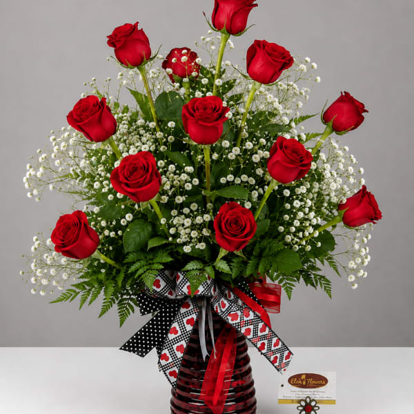 Red roses arranged in a red glass vase with white filler flowers
