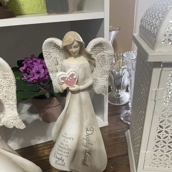 Decorative angel figurine with a heart, beside a small purple flower arrangement.
