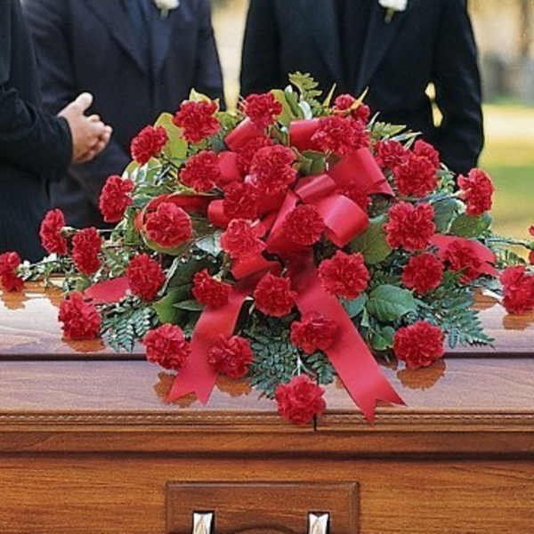 Red carnation casket spray with ribbon on a wooden casket