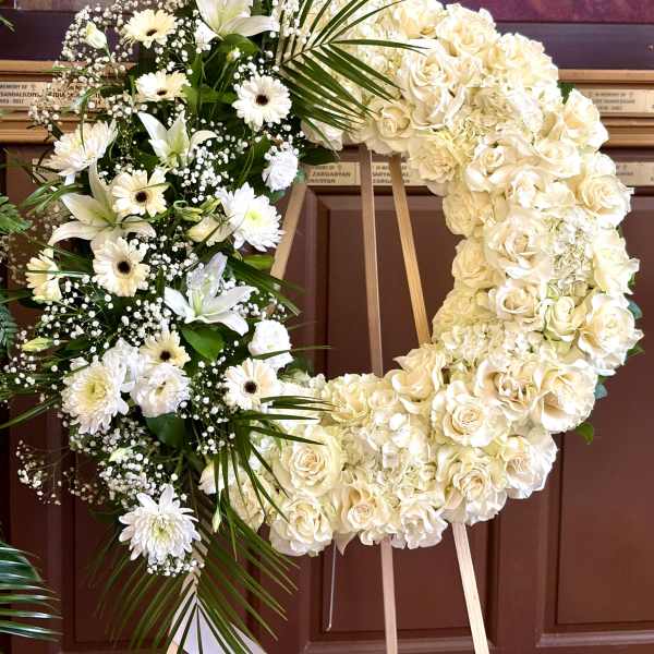 Large white floral wreath on an easel with roses and lilies