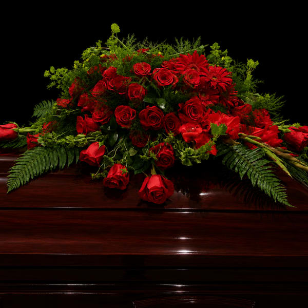 Red rose casket spray with greenery on a dark wood casket