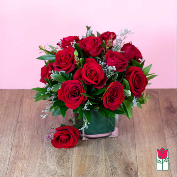 Red rose bouquet in a square glass vase on a wooden surface