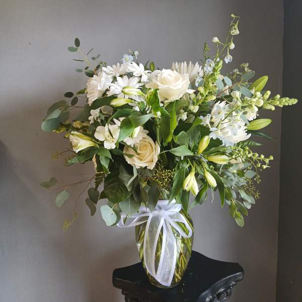 White roses and mixed white flowers in a glass vase with a ribbon