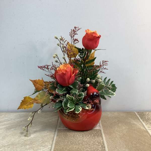 Two red-orange roses in a red ceramic vase with autumn leaves
