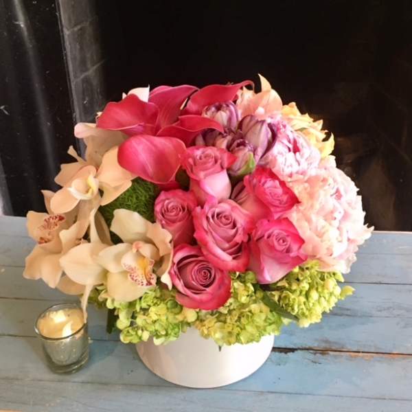 Pink roses and orchids arranged in a white vase with a small candle beside it.