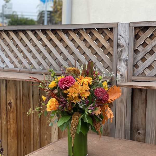 Autumn bouquet of orange, yellow, and pink flowers in a tall glass vase