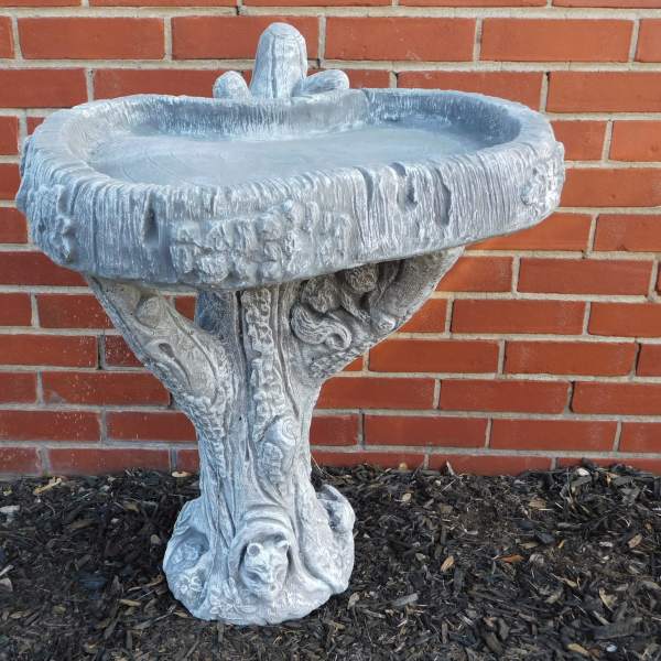 Stone birdbath with an ornate pedestal against a brick wall