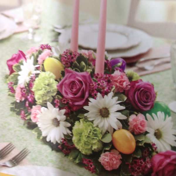 Pink floral centerpiece with two tall candles on a table
