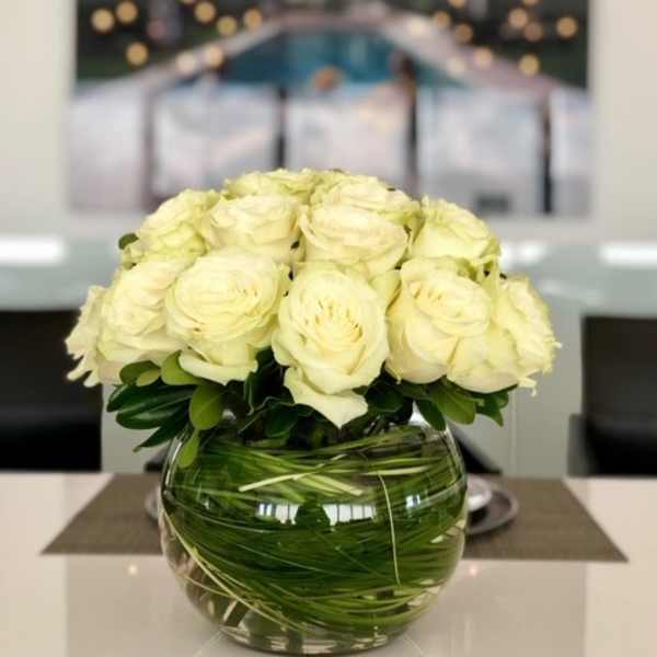 White roses arranged in a round glass vase with green stems visible inside
