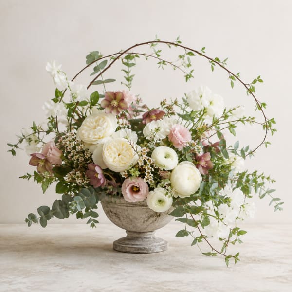 Pastel floral arrangement in a stone urn with arching branches