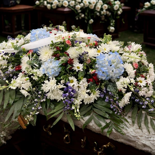 Large white floral casket spray with blue hydrangeas and purple accents
