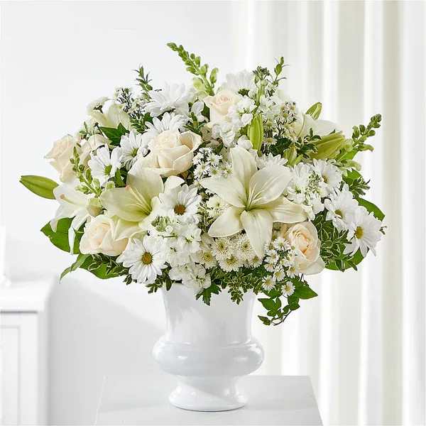 White floral arrangement in a white vase with roses, lilies, and daisies