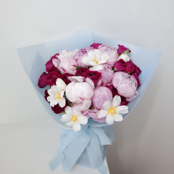 Bouquet of pink peonies and white flowers wrapped in pale blue paper