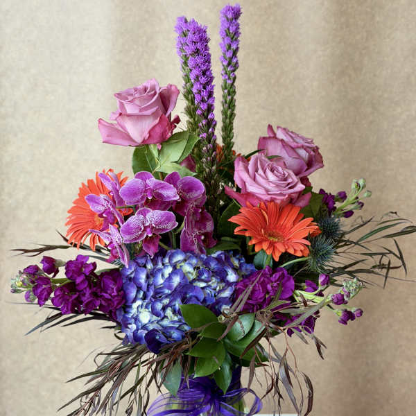 Mixed bouquet with pink roses, purple orchids, blue hydrangea, and orange gerbera daisies in a glass vase