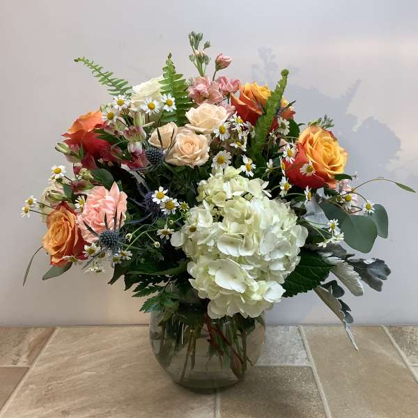 Mixed bouquet of roses, hydrangea, and daisies in a glass vase