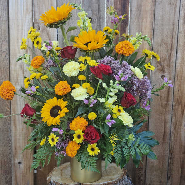 Mixed bouquet of sunflowers, roses, and marigolds in a gold vase