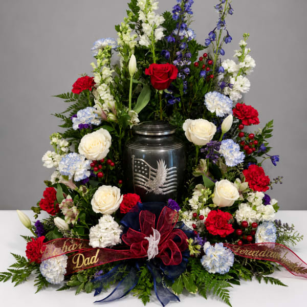 Standing floral tribute with red, white, and blue flowers around an urn