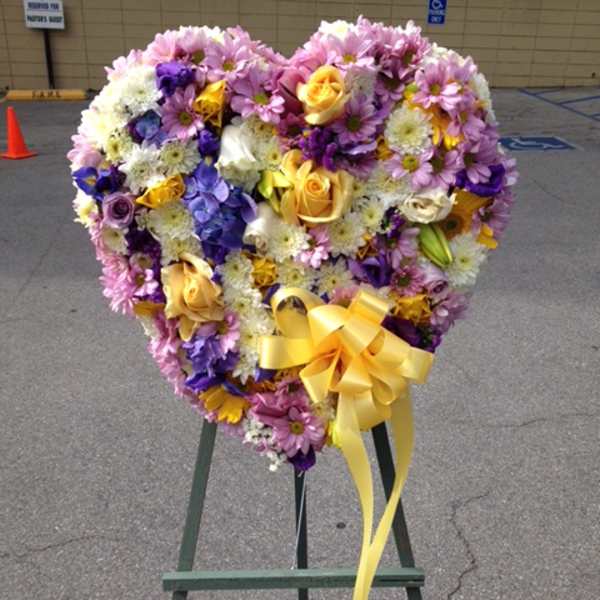 Heart-shaped floral wreath with a yellow ribbon on an easel