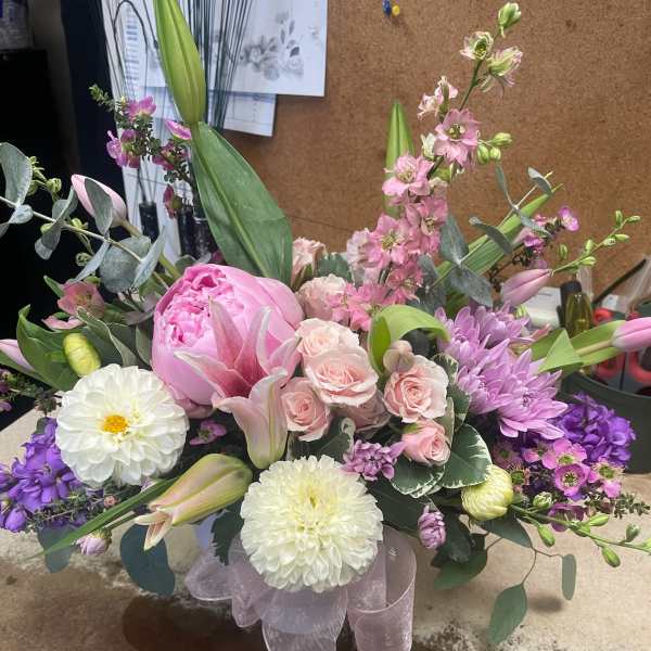 Pink and purple mixed flower arrangement with lilies and roses in a ribboned base