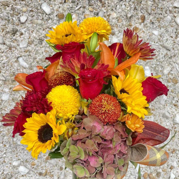 Bouquet of red roses, yellow sunflowers, and orange blooms in a glass vase