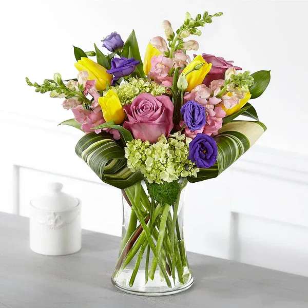 Mixed bouquet of pink, purple, and yellow flowers in a clear glass vase