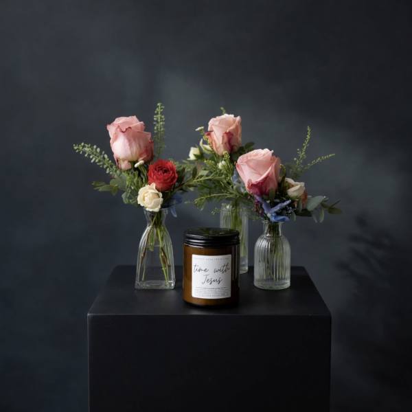 Three small rose arrangements in glass vases with a candle in front