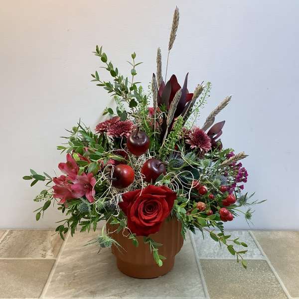 Red rose arrangement in a brown pot with apples and dried wheat