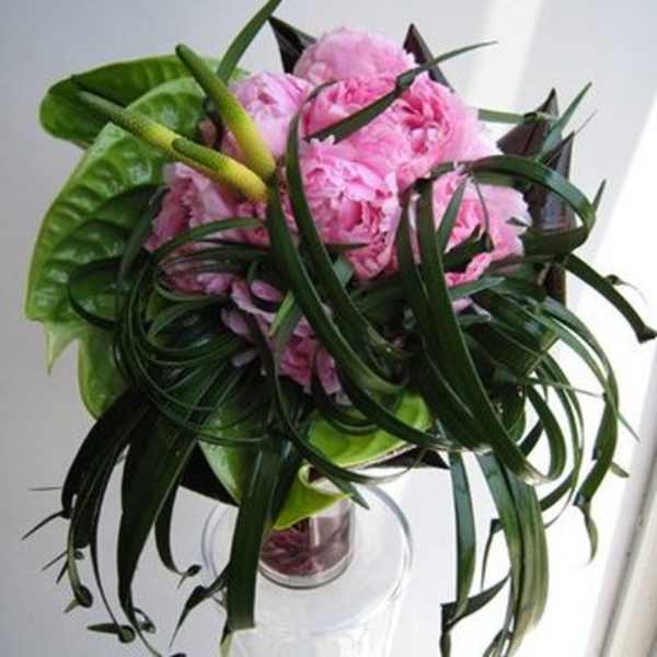 Pink peonies arranged with long dark green leaves in a clear glass vase