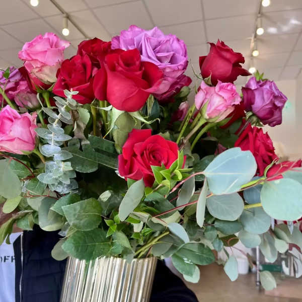 Bouquet of red, pink, and purple roses in a tall metallic vase
