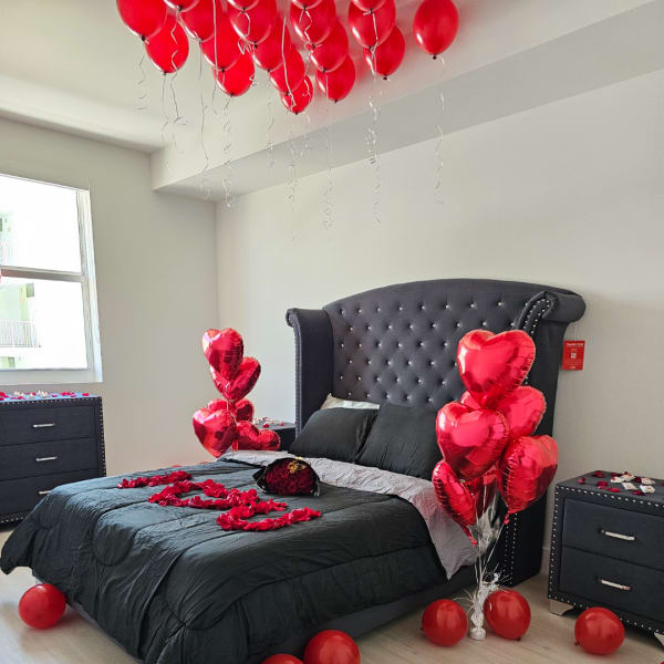Bedroom decorated with red heart balloons and rose petals on the bed